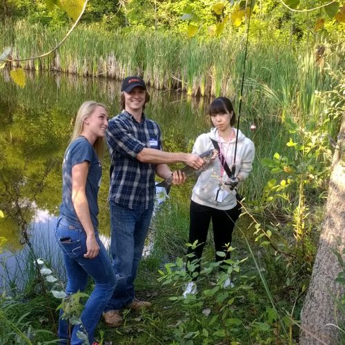 Three students holding a fishing rod and fish